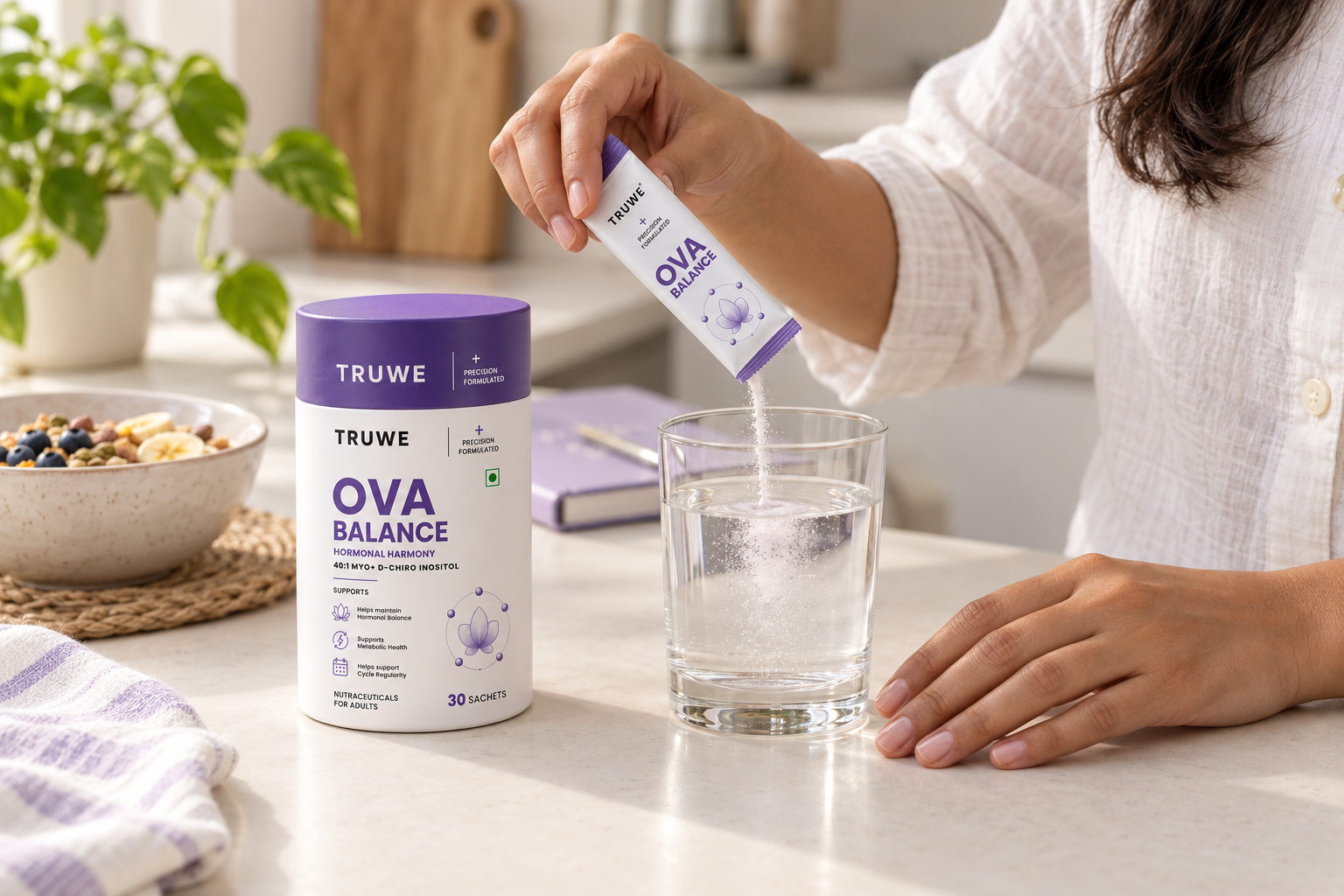 A woman pouring a TruWe Ova Balance sachet into a glass of water on a kitchen counter, beside the 30-sachet pack.